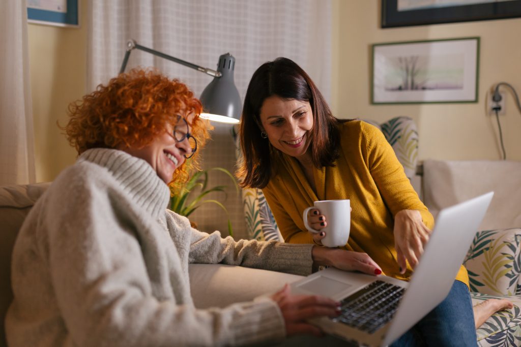 Two friends having fun at home on their laptop