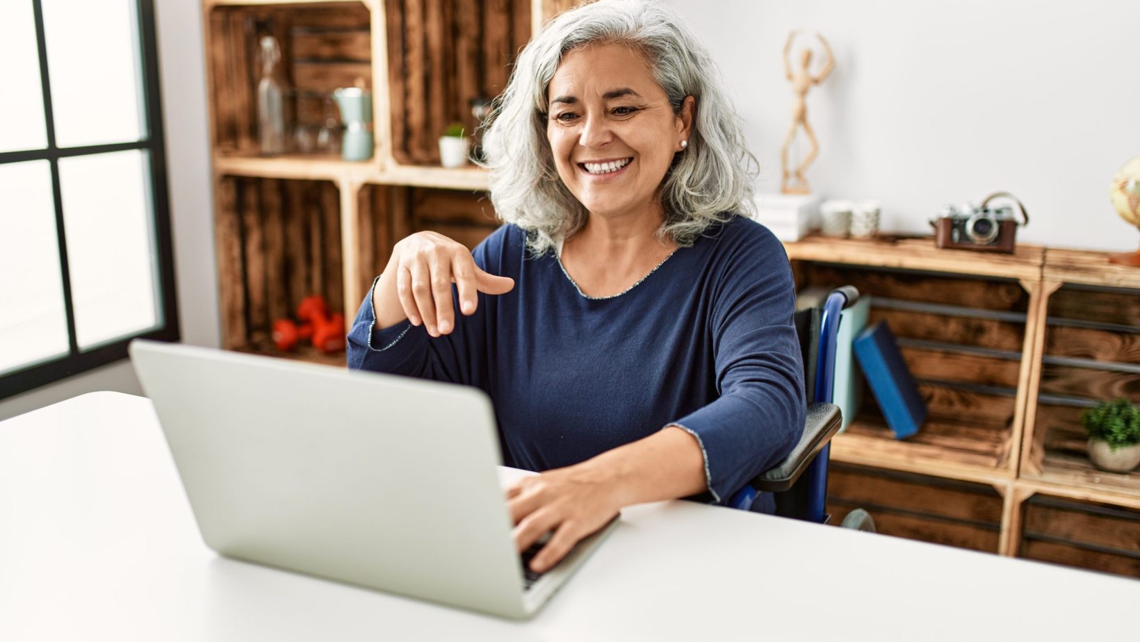 Woman smiling while using laptop sitting on wheelchair at home.